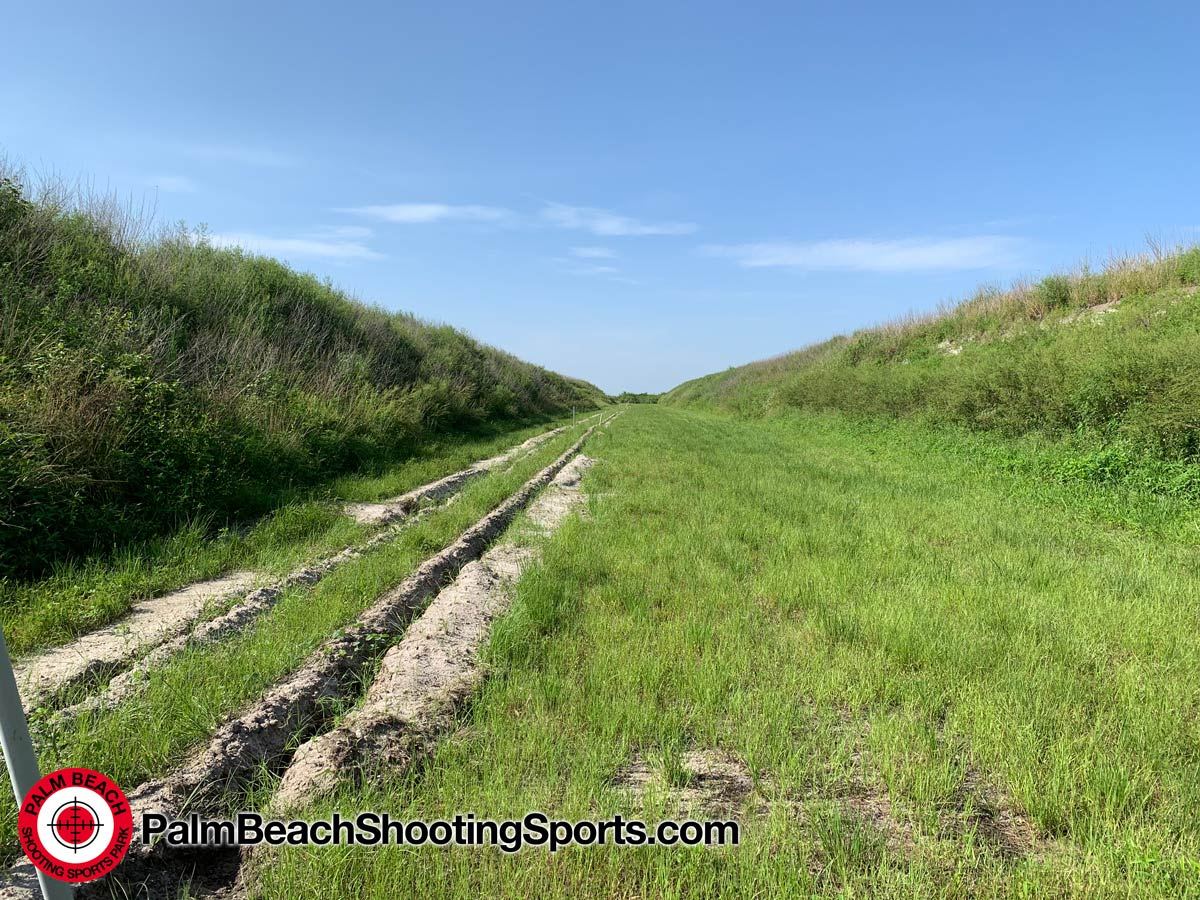 A long grass range between high grassy earth berms, with tracks from construction vehicles