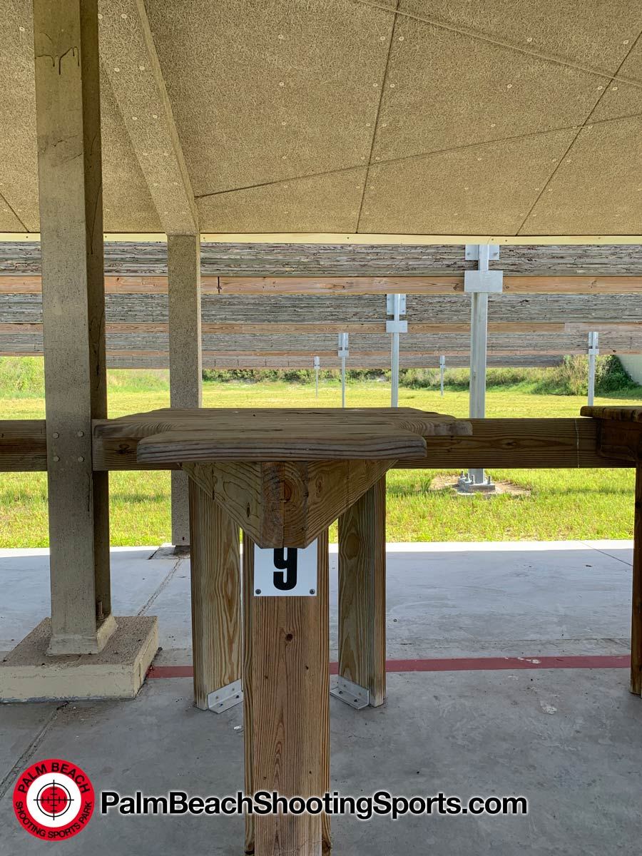 View from a numbered shooting bench under a roof looking out to target frames on a grass range