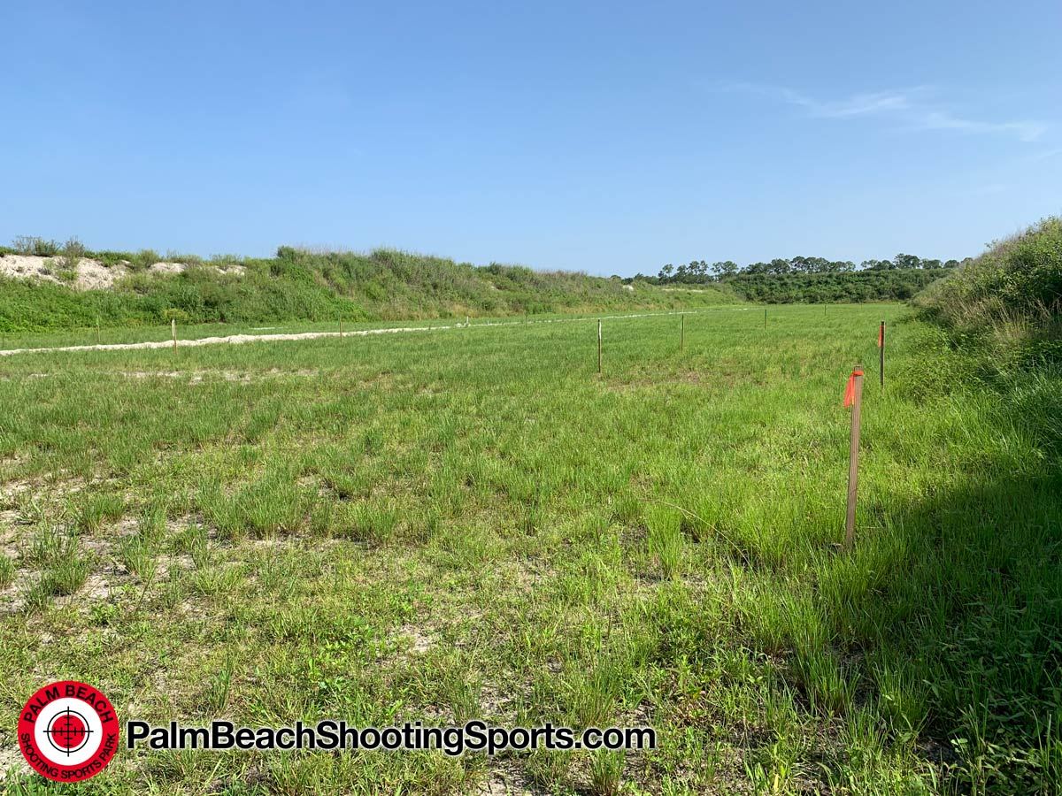 A grass range with orange survey stakes and a berm in the distance