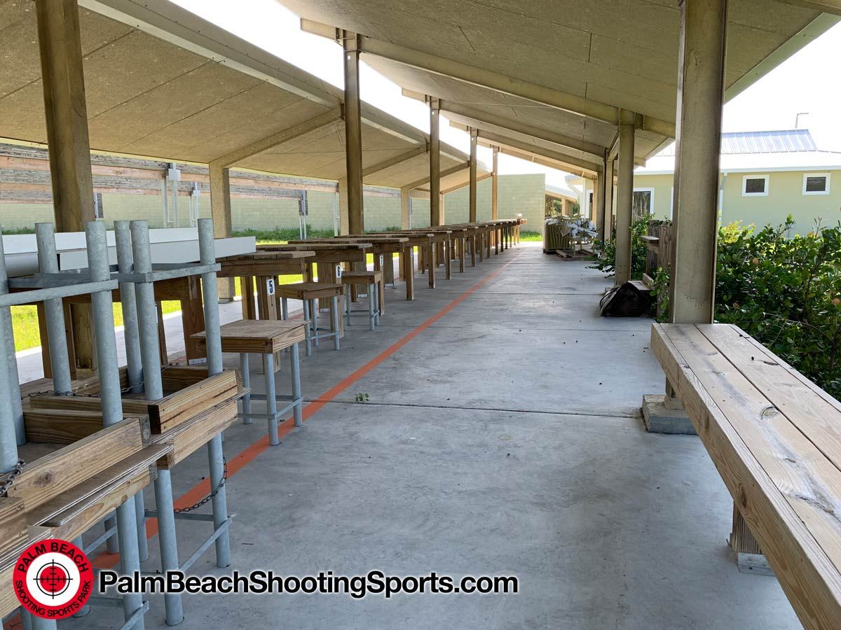 Rows of wooden shooting benches under a long covered firing line, with a red safety line painted on the concrete floor